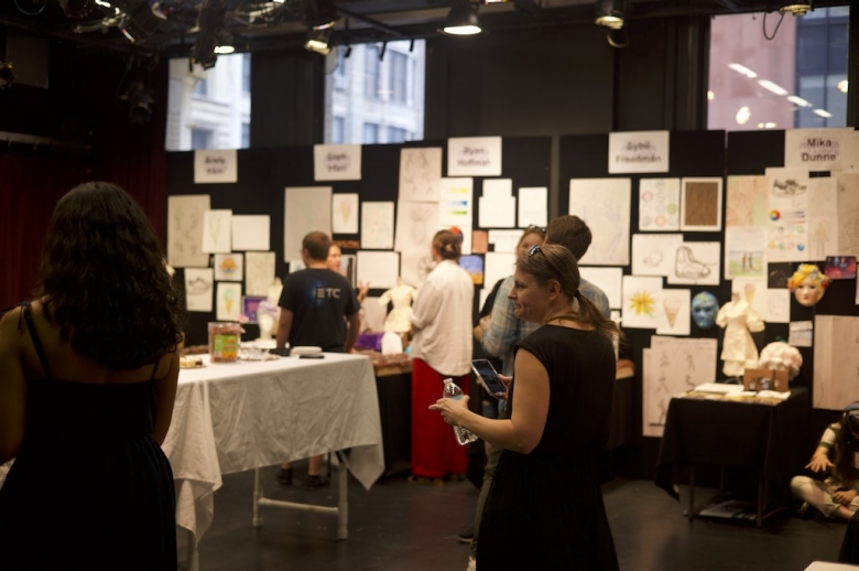 People viewing the Drama: Production & Design students' final projects, which include visual art pinned to a black fabric wall, costumes, and face masks.